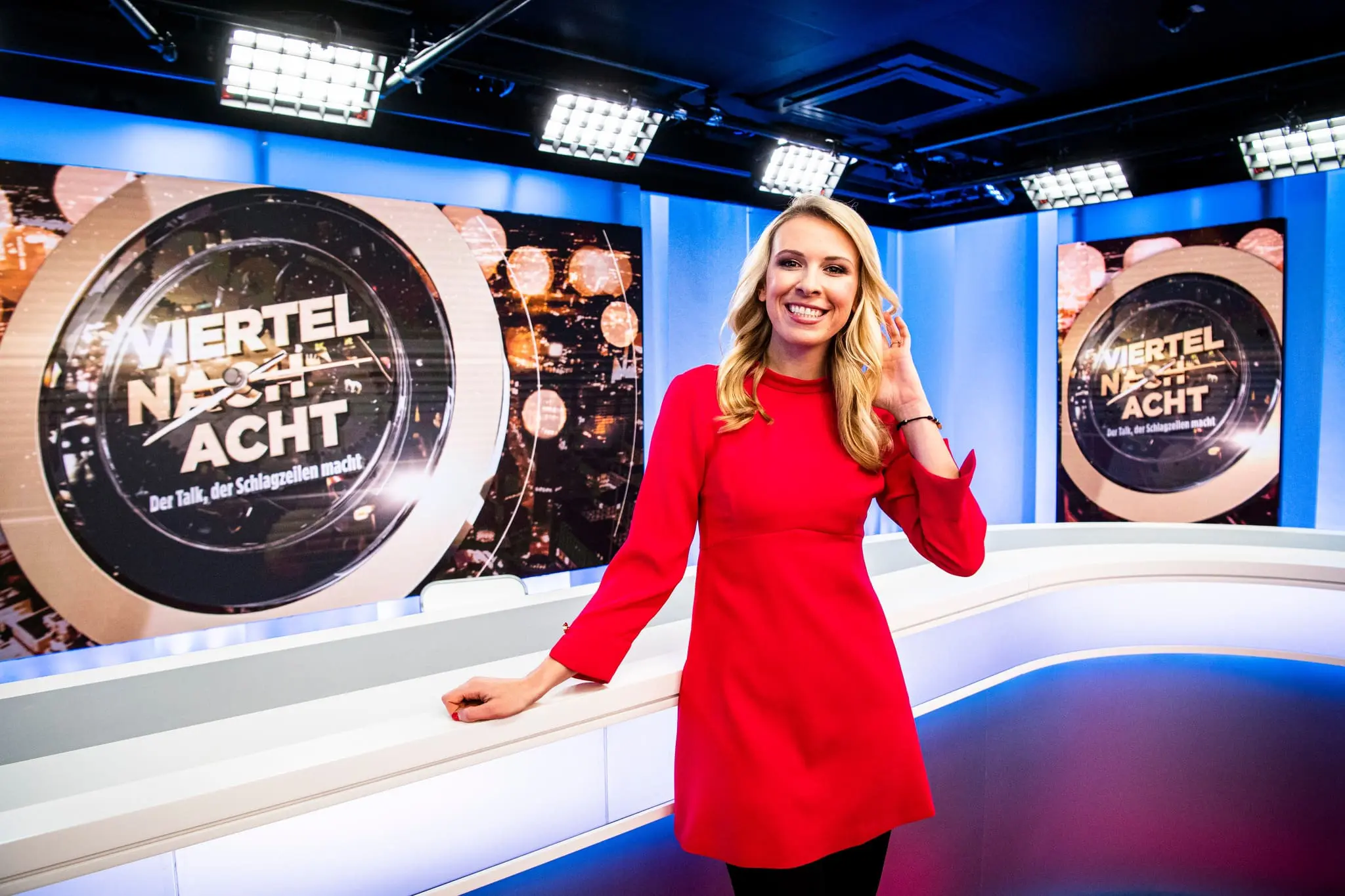 Moderatorin Nena Brockhaus im TV-Studioformat Viertel nach Acht, lächelnd vor dem beleuchteten Studiotisch und den großen Hintergrundscreens.
