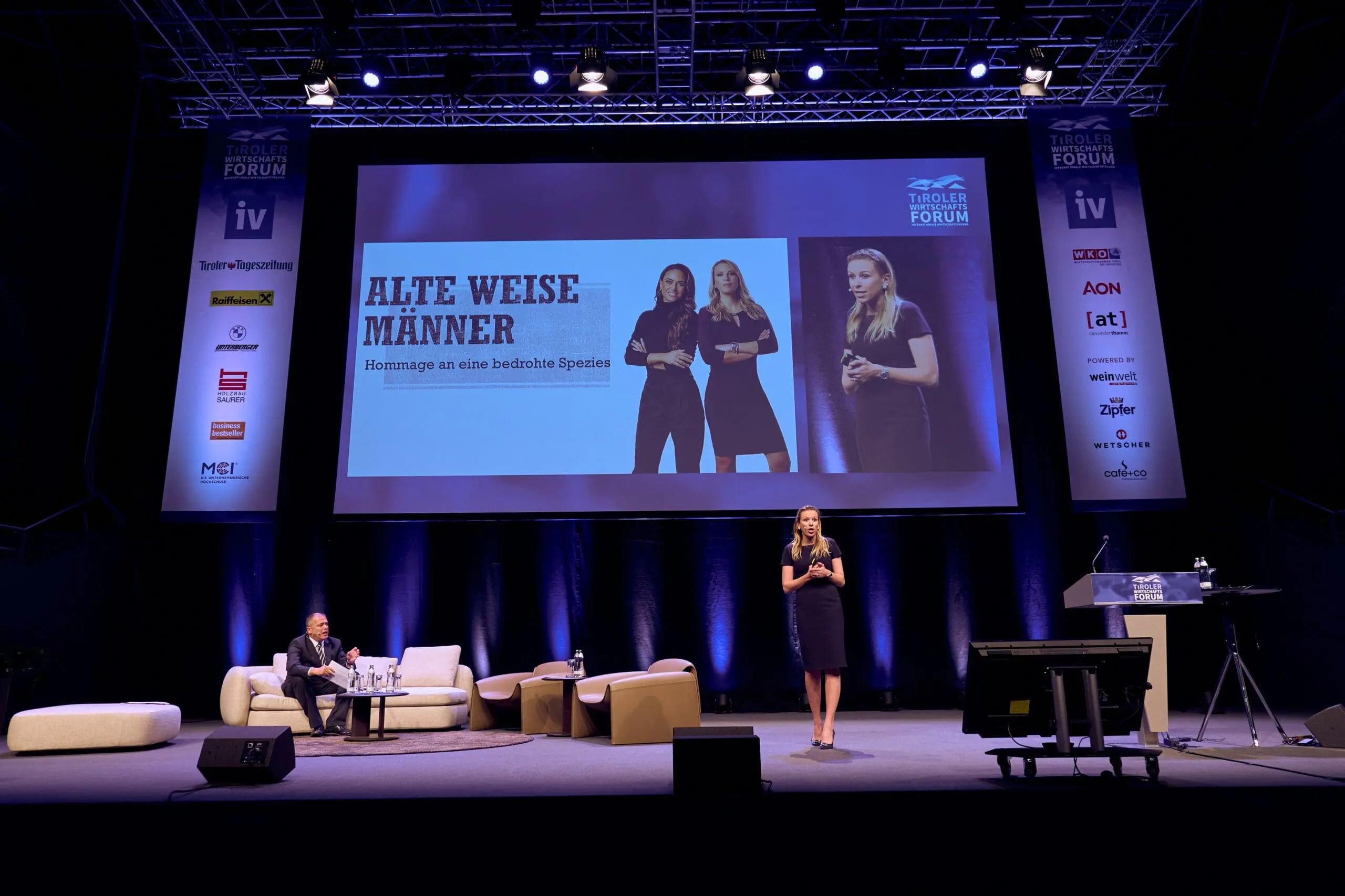 Speakerin Nena Brockhaus hält auf einer großen Bühne einen Vortrag; hinter ihr ist eine Präsentationsfolie mit dem Buchtitel Alte weise Männer zu sehen.